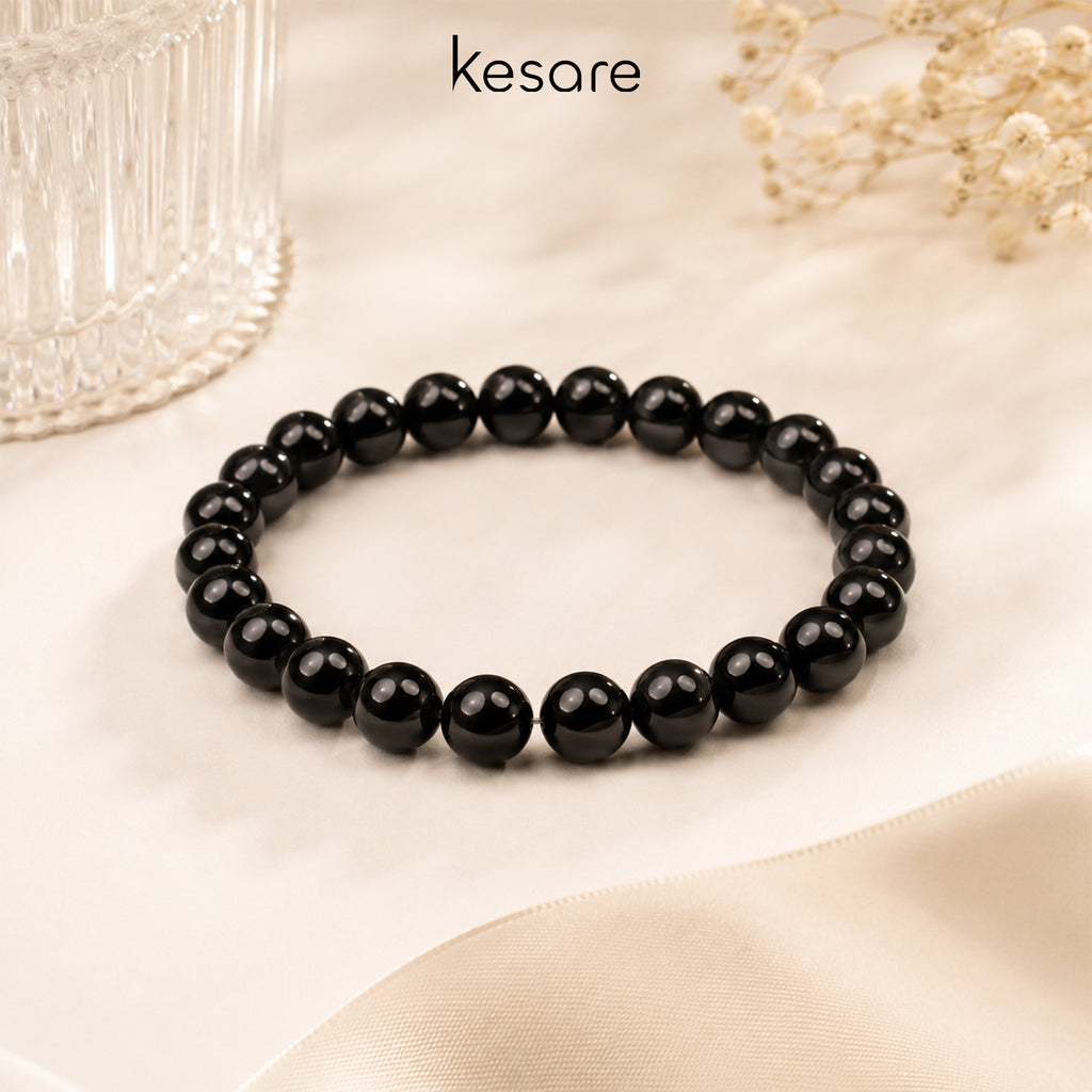 Black beaded bracelet on a beige surface with 'kesare' branding.