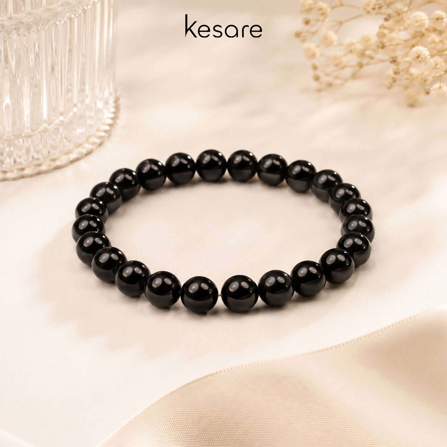 Black beaded bracelet on a beige surface with 'kesare' branding.