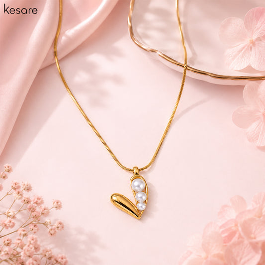 A gold chain necklace with a heart-shaped pendant featuring white faux pearls, styled on a soft pink background with decorative flowers and draped satin.