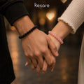Two hands holding each other with Kesare black and pink bracelets, blurred background