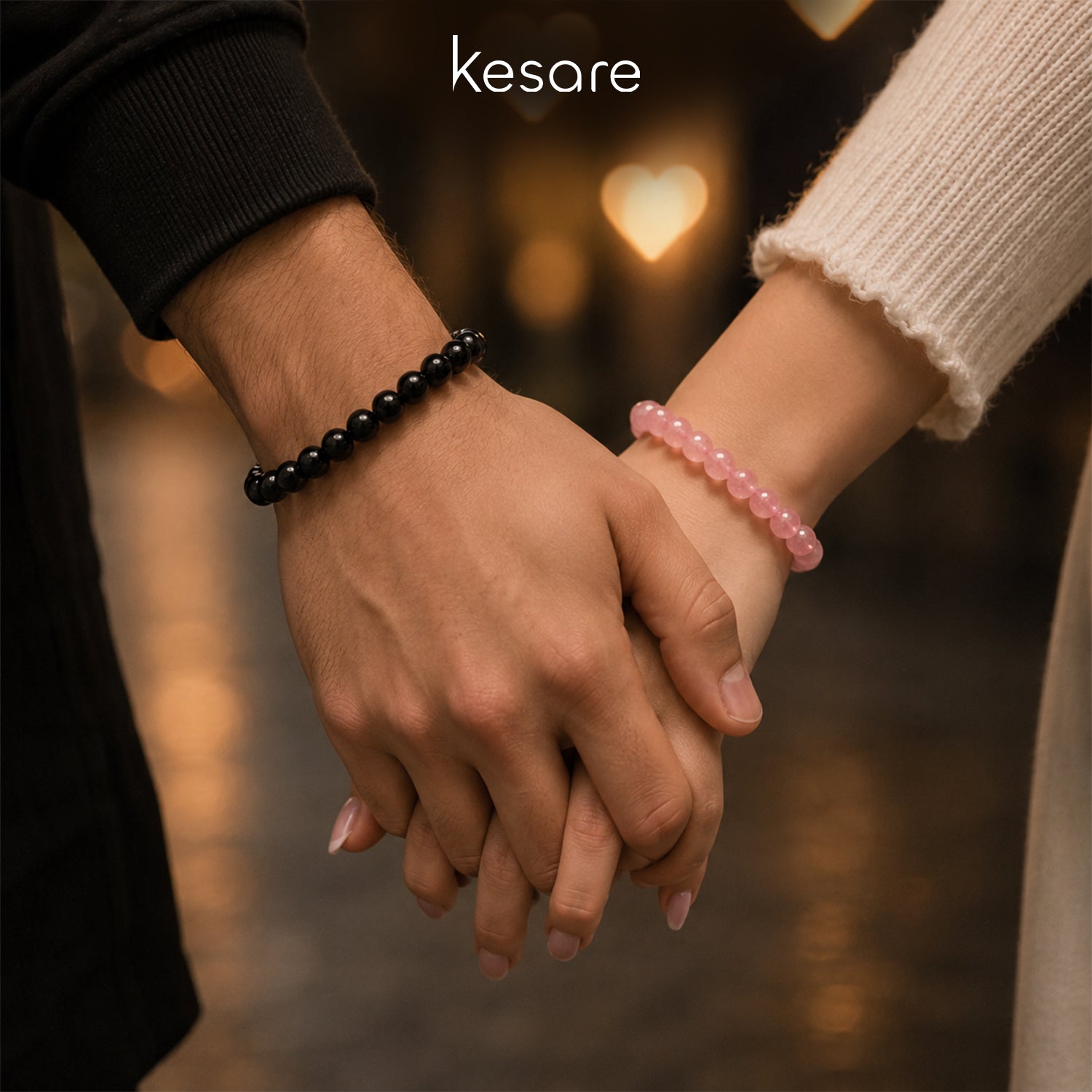 Two hands holding each other with Kesare black and pink bracelets, blurred background